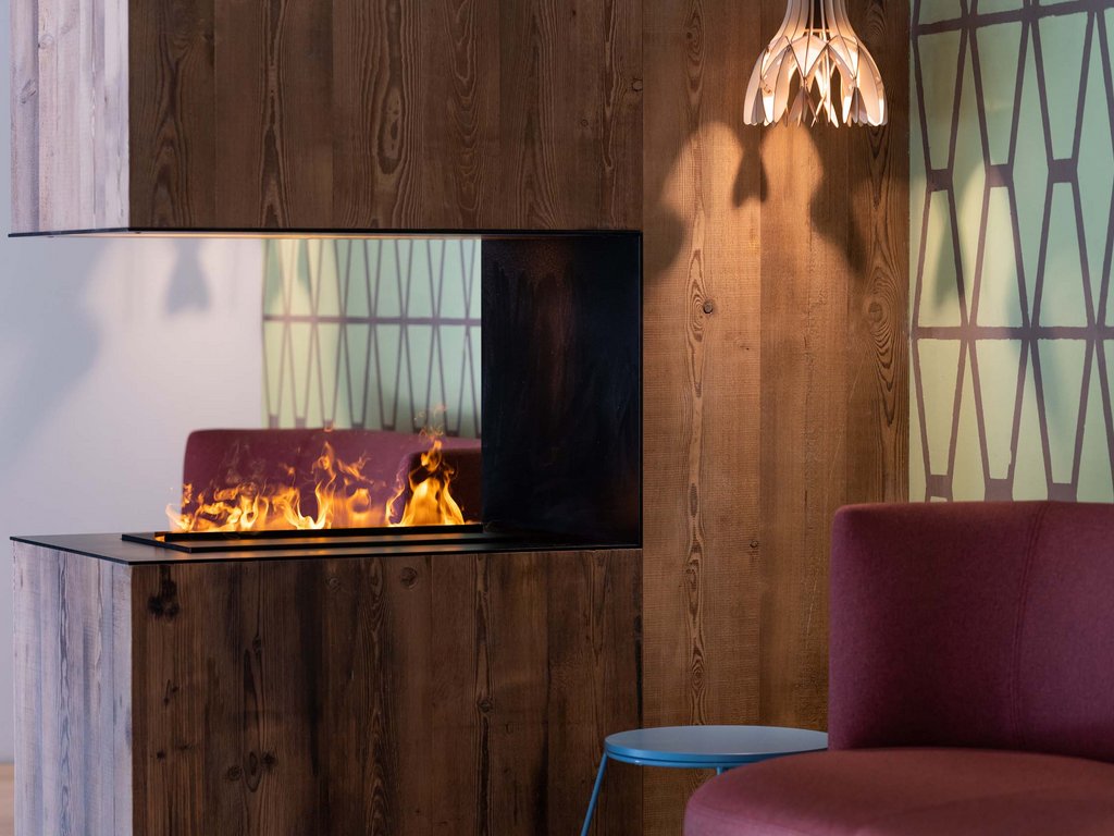In Soraga, the weather is always right for a day spa! Modern fireplace with visible flame, wooden wall, and red armchair