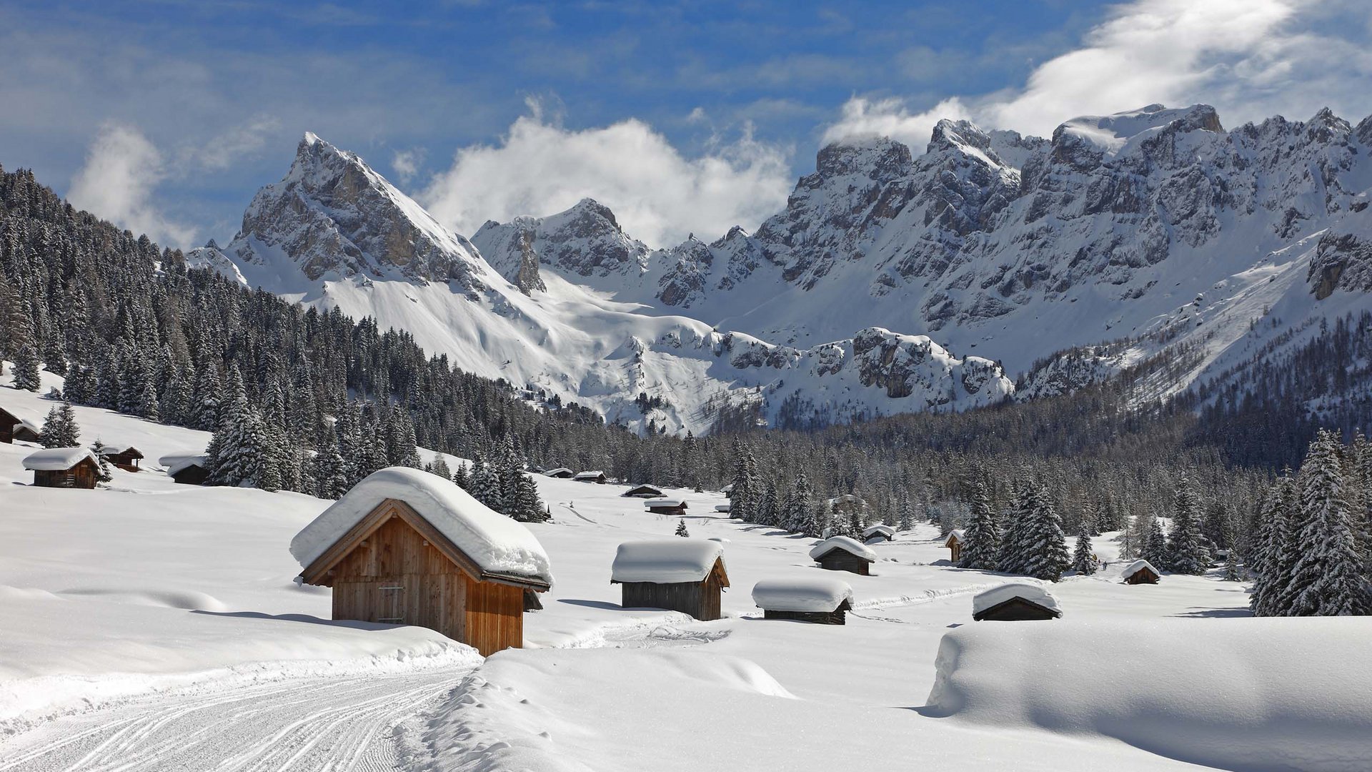 Val di Fassa: dove dormire e vivere vacanze sostenibili Paesaggio innevato con baite di legno e montagne sullo sfondo