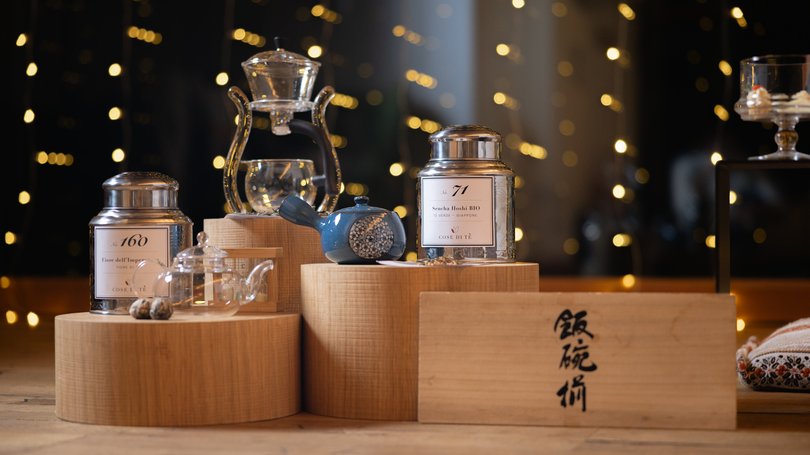 Val di Fassa: wandern, biken, erleben Teedosen, Teekannen und Zubehör auf Holzpodesten mit unscharfen Lichtern im Hintergrund