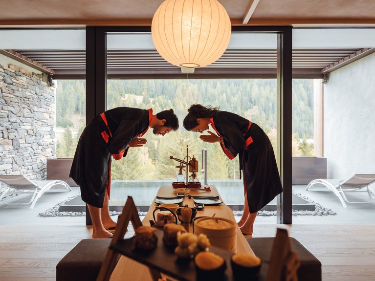 Urlaub im Fassatal: Erholung pur Paar in Kimonos verbeugt sich bei einer Teezeremonie in einem Raum mit Bergblick