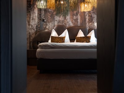 Barrierefreies Hotel im Val di Fassa: das Latemar Modernes, schwach beleuchtetes Schlafzimmer mit dekorativen Hängelampen und großem Bett.