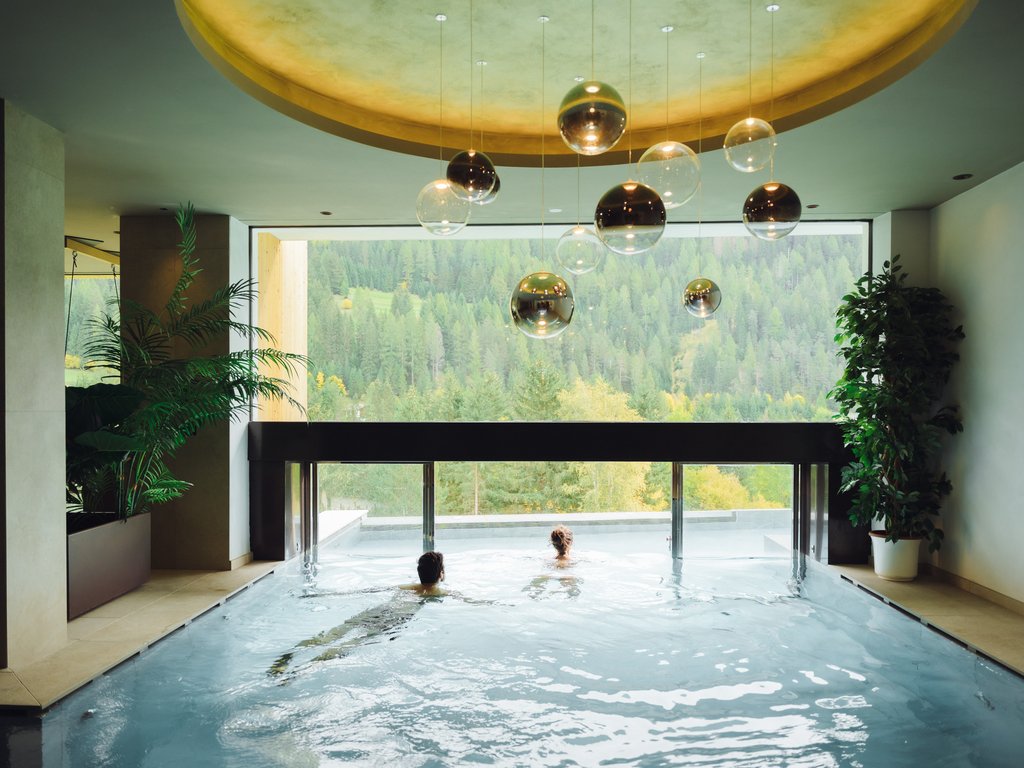 Al Latemar, dopo le passeggiate: relax nella Spa Oniro Persone che nuotano in piscina interna con vista sulle montagne verdi