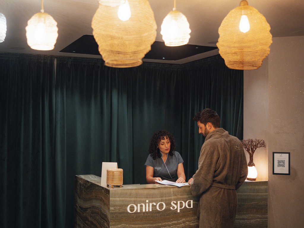 Trentino: Hotel am See mit Pool und Spa Gast im Bademantel an der Rezeption des Oniro Spa mit Empfangsdame