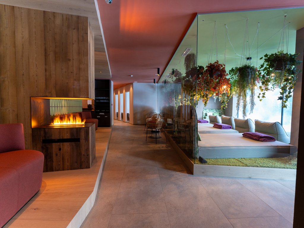 Soraga: dal lago alla piscina del Latemar Interno di una spa con camino, sedute rosse e area relax con piante sospese