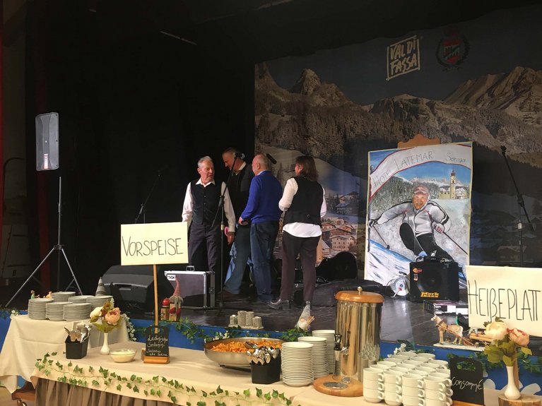 On the webcam Latemar is lovely, in real life it’s a dream! Buffet with plates, cups, and decorations in front of a stage with people