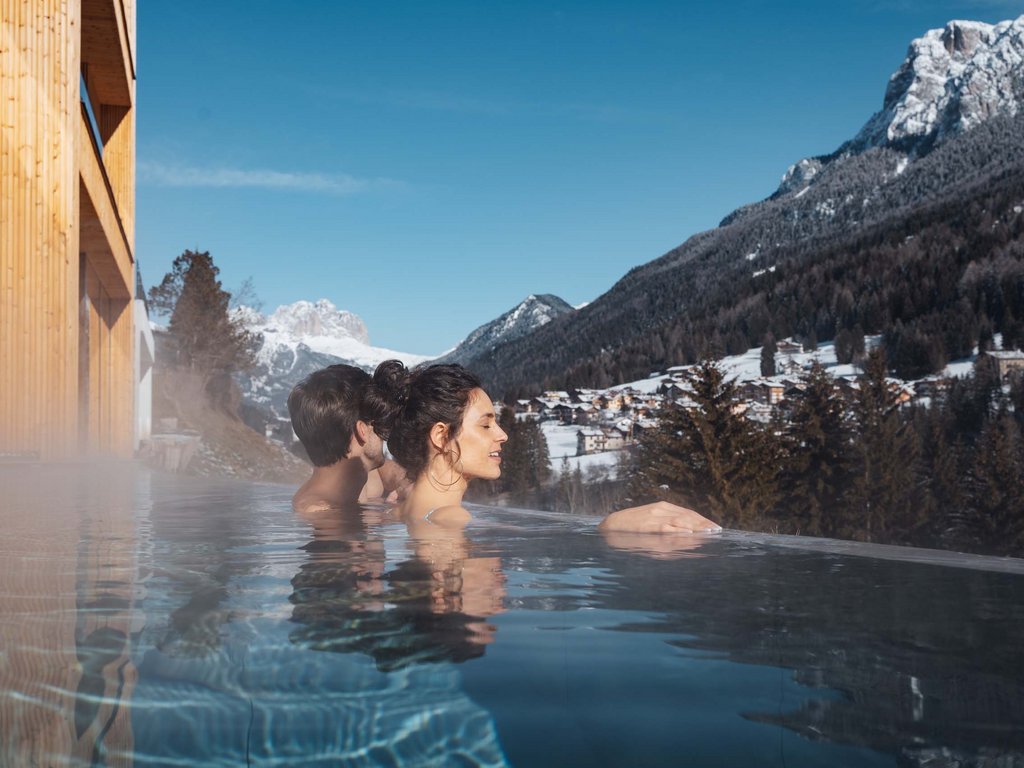 Al Latemar, dopo le passeggiate: relax nella Spa Oniro Persone che si rilassano in piscina con vista sulle montagne innevate