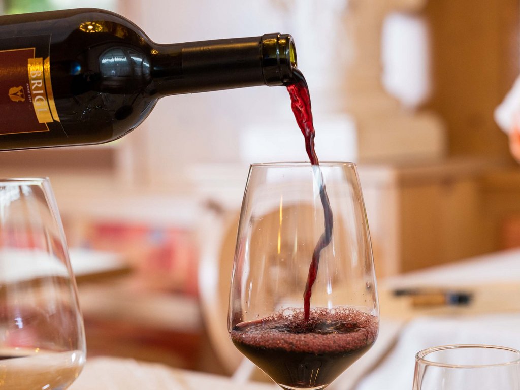 In Val di Fassa in inverno e in estate si brinda col vino! Vino rosso versato da bottiglia in un calice su un tavolo apparecchiato