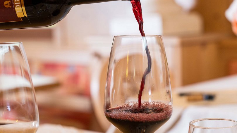 Val di Fassa: wandern, biken, erleben Rotwein wird von Flasche in Glas an gedecktem Tisch gegossen