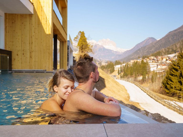 Sulla pista ciclabile, da Moena alla vostra oasi romantica Coppia che si rilassa in piscina con vista sulle montagne innevate