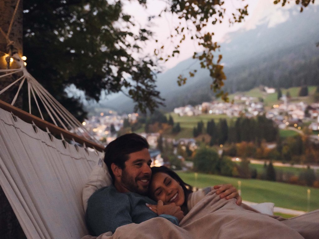 Sulla pista ciclabile, da Moena alla vostra oasi romantica Coppia che si abbraccia in un'amaca con vista panoramica al tramonto