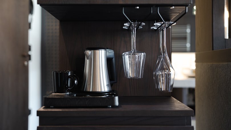 Moena: Unterkunft für Ihren Traumurlaub. Hotel Latemar! Kaffeemaschine mit schwarzer Tasse und hängenden Gläsern in dunkler Küche