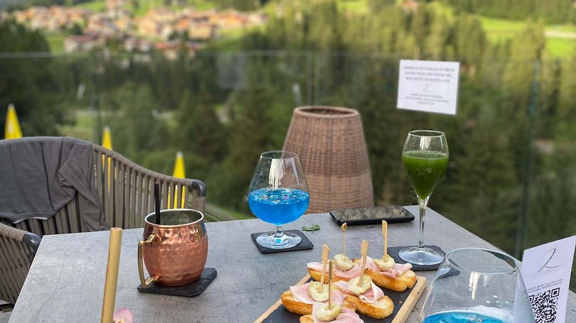 Val di Fassa: wandern, biken, erleben Tisch mit Aperitifs, Snacks und grünem Bergblick