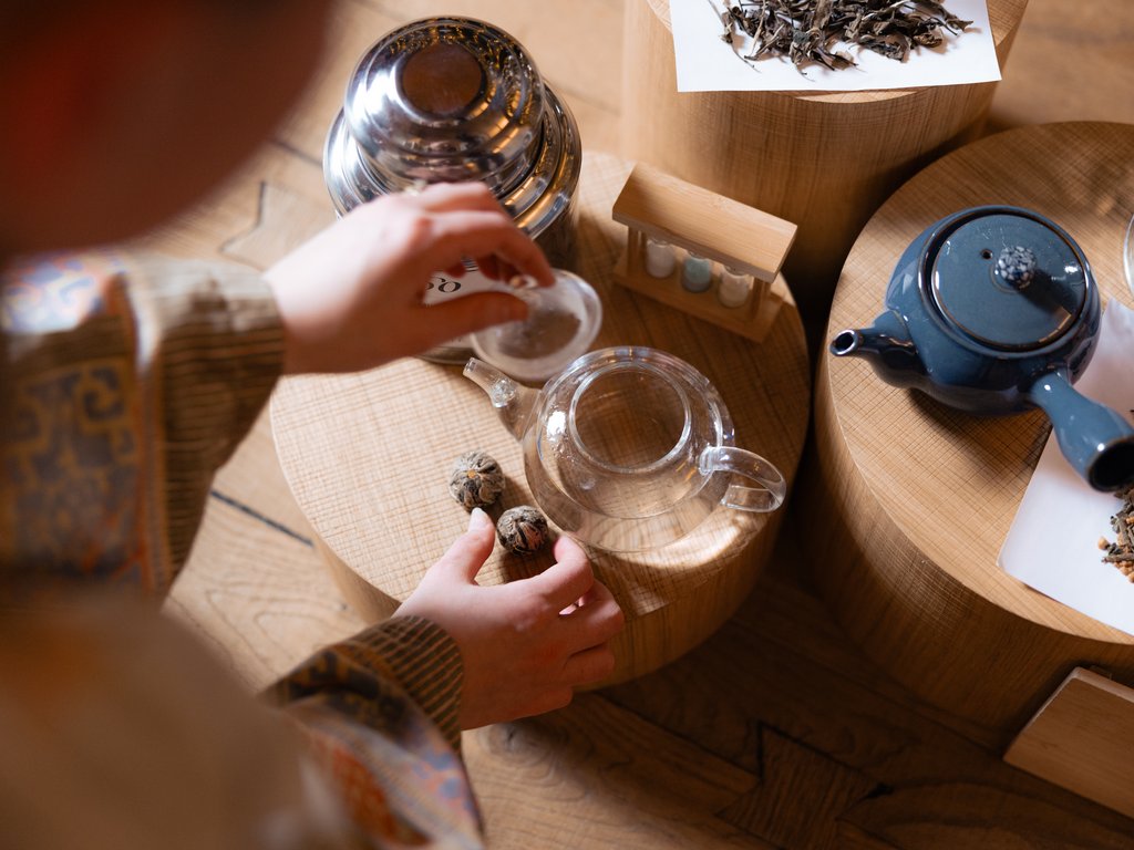 Per buongustai: l’hotel ideale vicino a Moena Persona che prepara il tè con teiere e sfere di tè su tavoli rotondi in legno