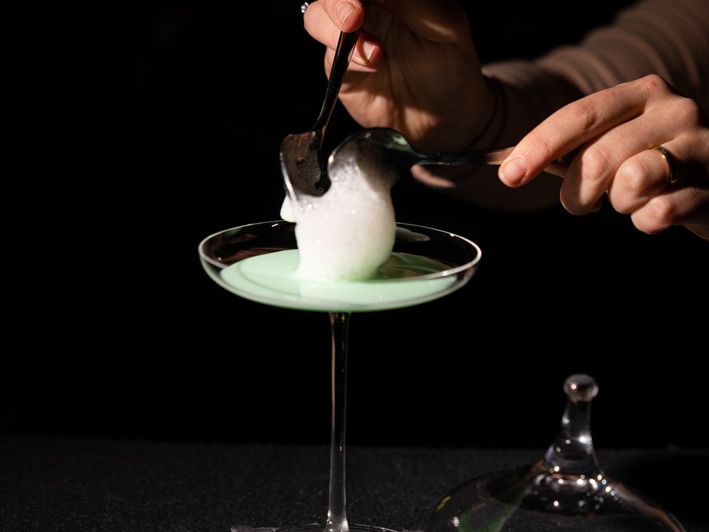 Val di Fassa and cycle track: outside our cocktail & tea bar Hand adding foam on green cocktail in a cocktail glass