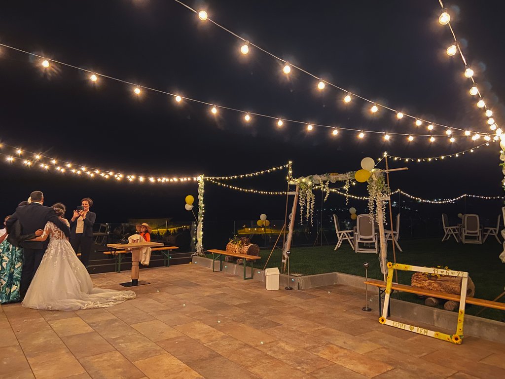 Dalla webcam il Latemar è bello, ma dal vivo è un sogno! Festa di matrimonio all'aperto di notte con luci decorative e persone che si fotografano