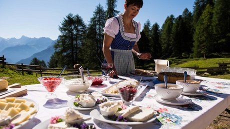 Picture gallery Woman in traditional dress setting food on outdoor table in mountain scenery