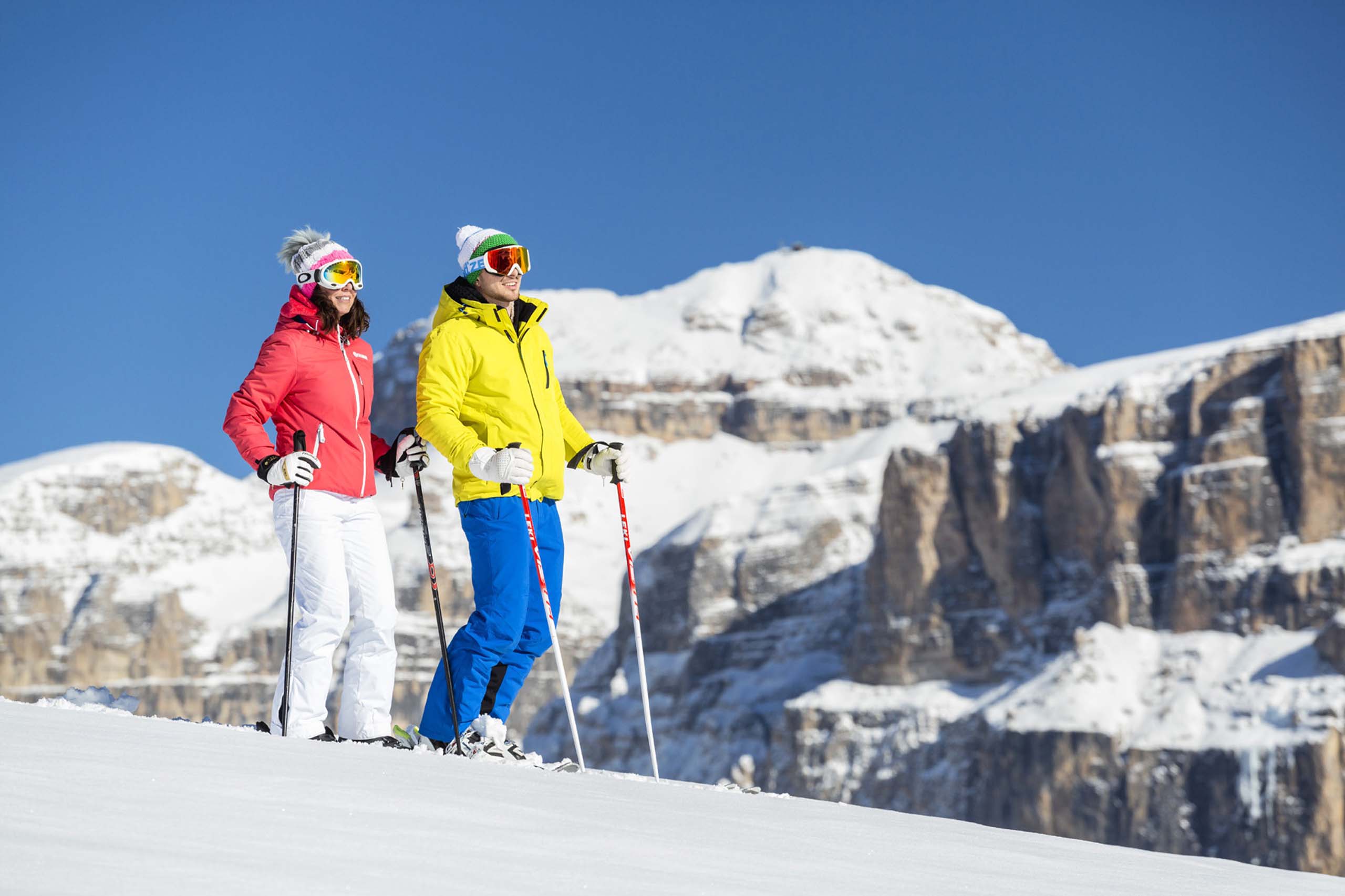 Hotel in Val di Fassa: your Hotel Latemar Couple of skiers in colorful outfits on snow with snowy mountains in background